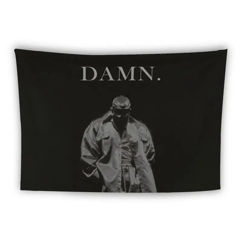 A black tapestry with a monochrome image of a person wearing a loose jacket and cap, standing with hands in pockets. The large text "DAMN." is printed above the figure. The background is solid black.