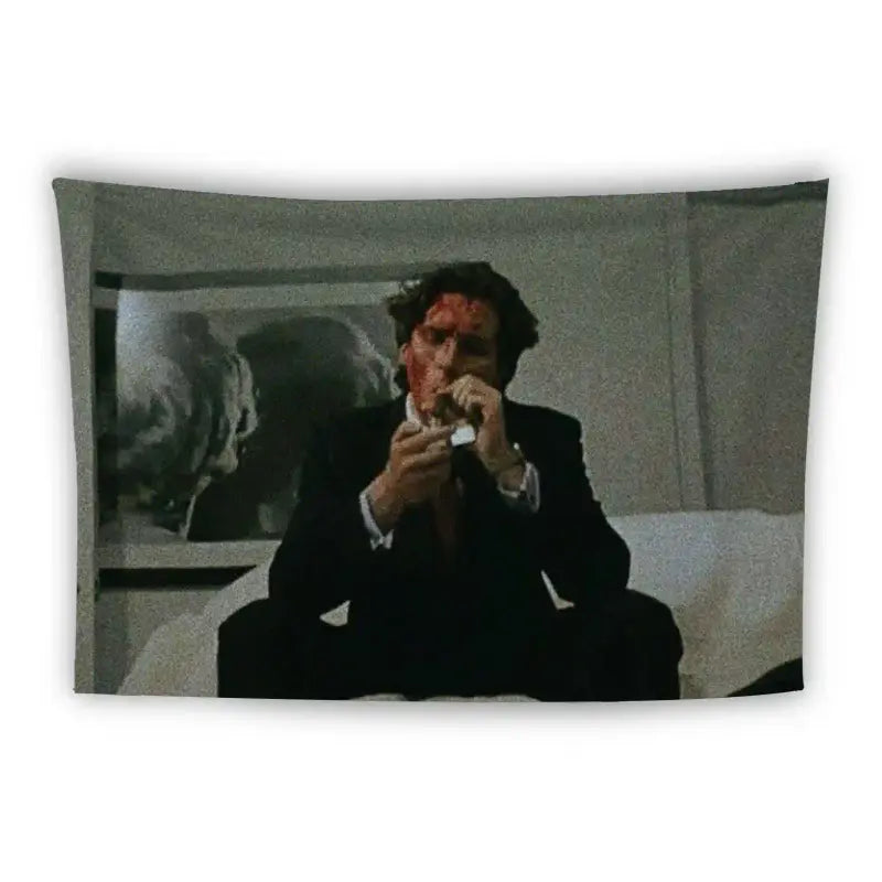 A man in a suit sits on a white couch in a dimly lit room with his face covered in blood. One of his hands is raised near his mouth, holding a tissue or small object. There's a painting of a large white flower on the wall behind him.