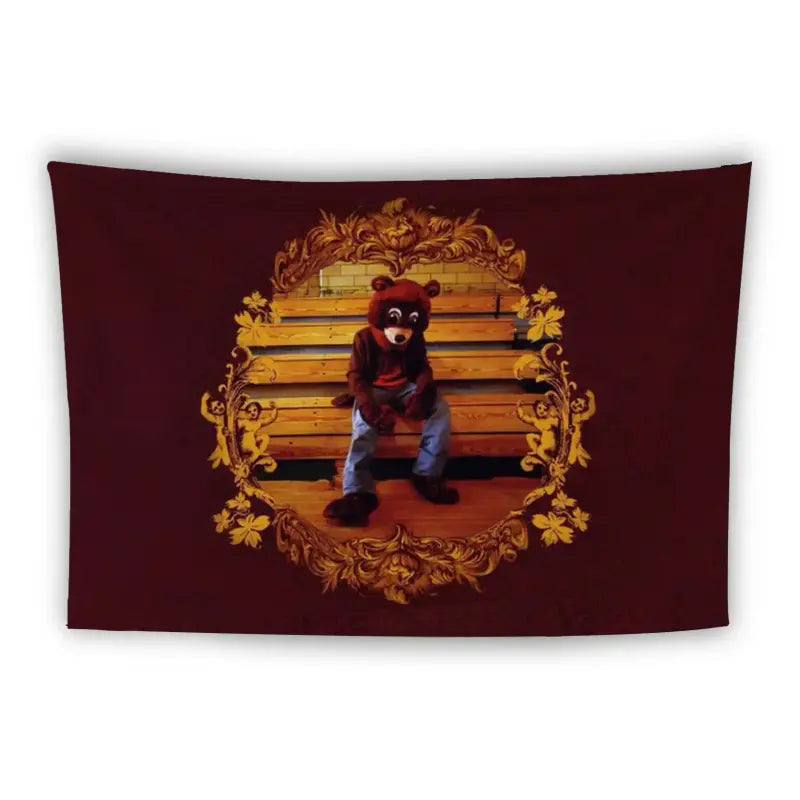 A tapestry featuring a bear wearing a red shirt and blue jeans, sitting on wooden bleachers. The bear is set against a maroon background with an ornate, golden floral frame surrounding it.