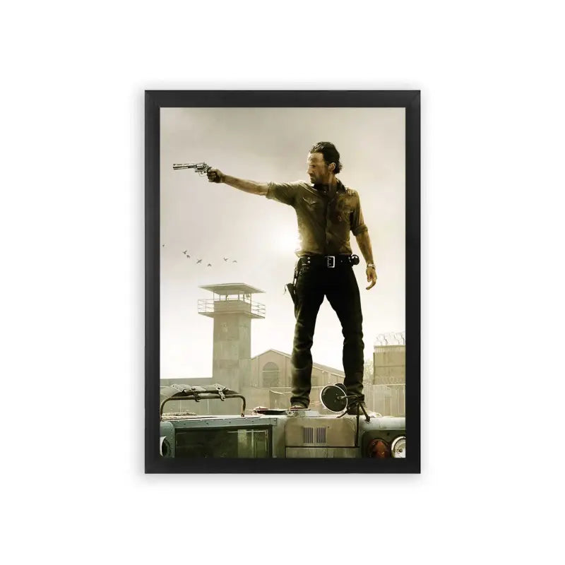 The Walking Dead 'Survivor's Stand' Framed Poster Black Premium Wood A rugged adventurer stands atop an overturned vehicle, confidently aiming a gun off to the distance, with a watchtower and birds in the dusky sky behind him.