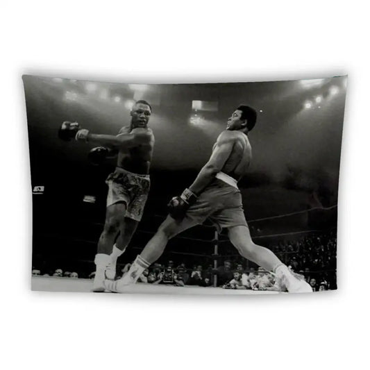 A black-and-white photograph captures an intense moment in a boxing ring. Two boxers are in the midst of delivering punches, with one boxer leaning back to dodge or absorb a hit from the other. Arena lights illuminate the scene, and the crowd is visible in the background.