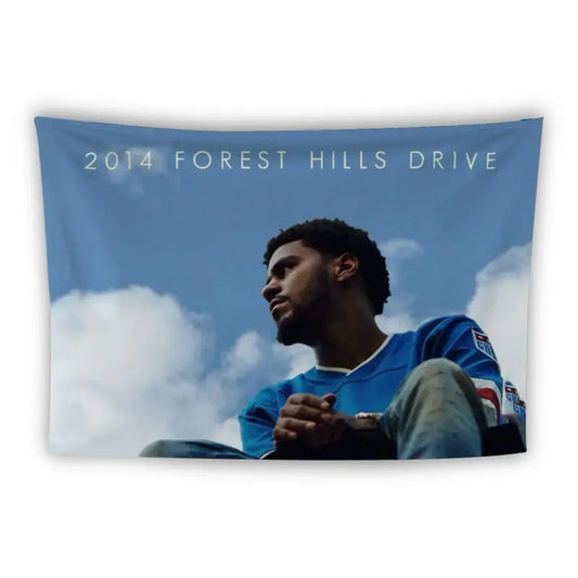 Tapestry featuring cover art from J. Cole's album "2014 Forest Hills Drive." The image shows a man sitting with arms crossed on his knees, looking contemplatively into the distance against a blue sky with clouds.